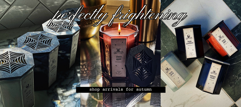 Candle collection with spider web designs on a reflective surface, featuring text 'perfectly frightening' and 'shop arrivals for autumn'.